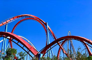 A red roller coaster in a amusement park with some loopings