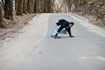 Street style arab man in eyeglasses with longboard longboarding down the road.