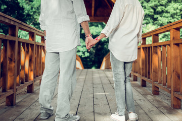 Close-up of spouses holding hands while standing on the bridge.
