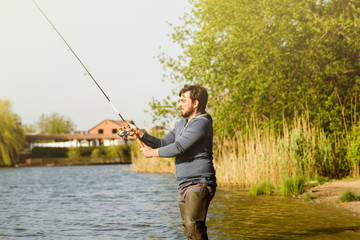 a man in boots standing in the lake and fishing on spinnin