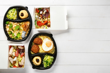 Containers with delicious food on white wooden background