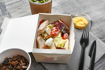 Container with delicious food on grey background