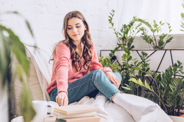 selective focus of attractive girl taking book while sitting in white soft chaise lounge at home