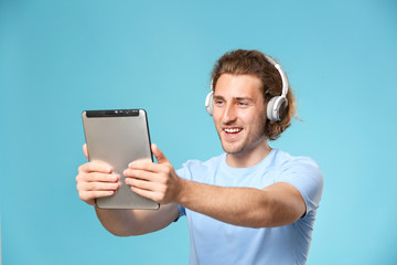 Handsome man with tablet computer and headphones on color background