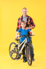 Father and his son with bicycle on color background