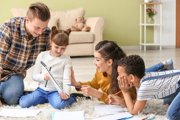 Happy couple with little adopted children drawing at home