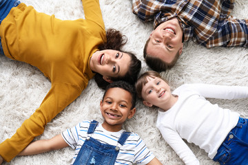 Happy couple with little adopted children lying on floor at home