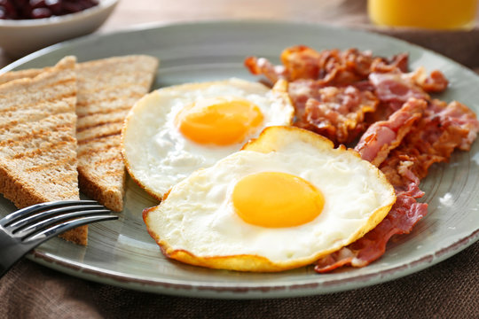 Plate with tasty fried eggs, bacon and toasts on table, closeup