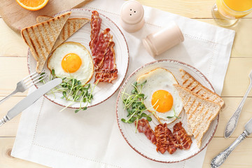 Plates with tasty fried eggs, bacon and toasts on table