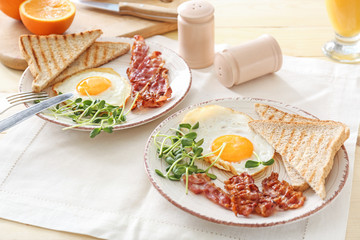 Plates with tasty fried eggs, bacon and toasts on table