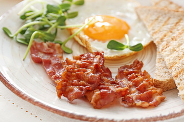 Plate with tasty fried egg, bacon and toasts on table, closeup