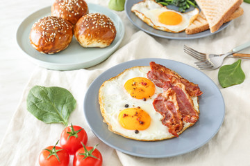 Composition with tasty fried eggs, bacon and buns on table