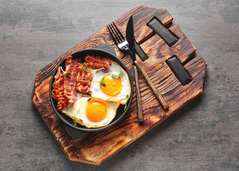 Frying pan with tasty eggs and bacon on grey background