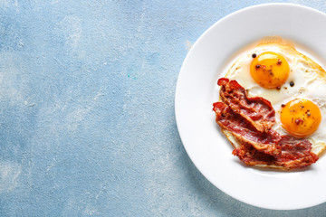 Plate with tasty fried eggs and bacon on color background