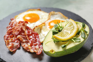 Slate plate with tasty fried eggs, bacon and avocado, closeup
