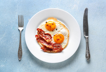 Plate with tasty fried eggs and bacon on color background