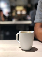 Black coffee in white cup on the wooden table with cafe light. Copy space