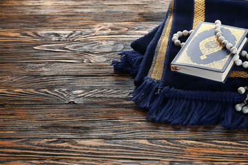 Muslim prayer mat, beads and Koran on wooden background