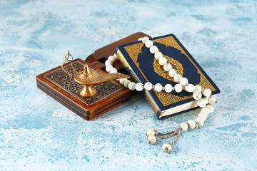 Koran, rehal, lamp and Muslim beads on color background