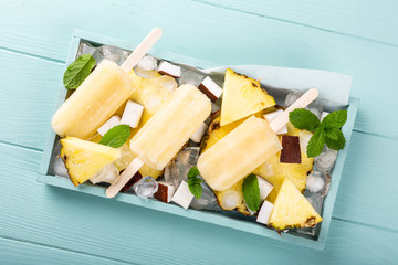 Overhead shoot for homemade pineapple coconut popsicles on turquoise background. Summer food concept flat lay with copy space. Top view.