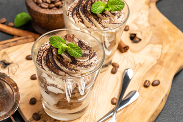 Classic tiramisu dessert in a glass on dark concrete background