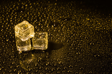 Ice cubes in yellow light on black wet table.