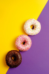 pink white and black chocolate donuts on yellow and violet deep purple background top view copy space