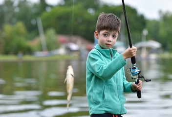 kid boy hold a fish on fishing rod