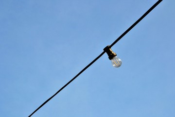 A string with one outdoor light bulb hanging against a clear blue sky. Light bulb on the sky background. 