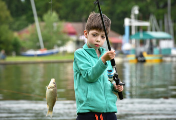 kid boy hold a fish on fishing rod