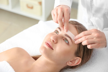 Fototapeta na wymiar Young woman undergoing eyebrows epilation in beauty salon