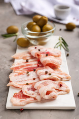 Board with fresh raw bacon and olives on table