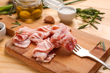 Fresh raw bacon and fork on wooden board