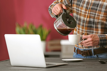 Handsome man with laptop drinking coffee at home, closeup