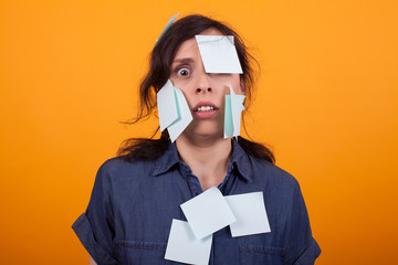 Portrait of cute young woman overwhelmed of work with sticky notes on her over yellow background in...
