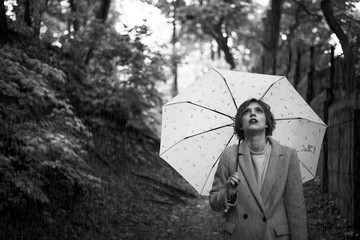 A sad beautiful girl is standing under an umbrella. Walk in the rain in the park. Black and white...