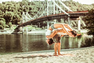 Active sporty young couple performing acroyoga asanas outdoors