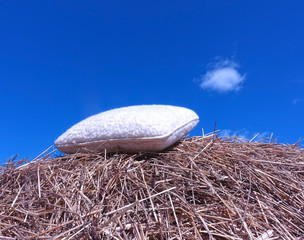 Sheepskin pillow on a stack of straw against a blue sky © Oksana