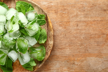 Plate with ice cubes and fresh mint on wooden background