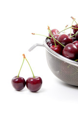 Steel colander with red sweet cherry isolated on a white background..