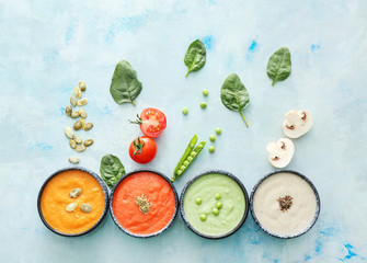 Bowls of different tasty cream soups on color background