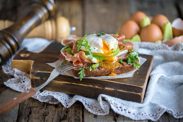 Toast with poached egg, prosciutto, arugula, cheese and avocado