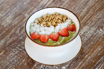 Delicious organic green smoothie bowl garnished with strawberries, sliced almonds and granola