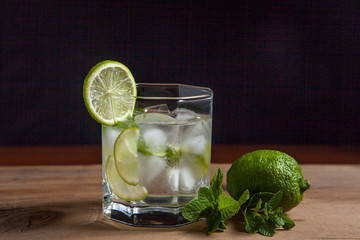 Summer cocktail mojito in glass, sliced lime and mint on wooden background..