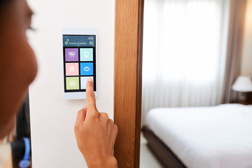 Close-up of woman touching the display and controlling smart home system hanging on the wall in her apartment