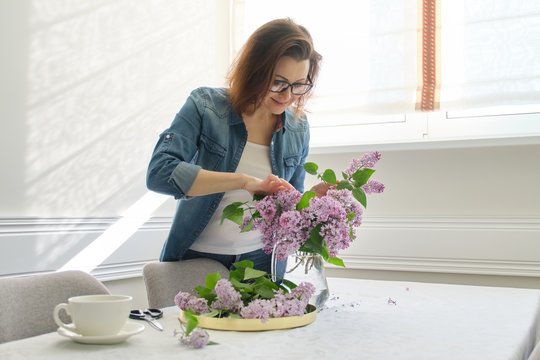 Mature Woman Making Bouquet Of Lilac Branches At Home At Table