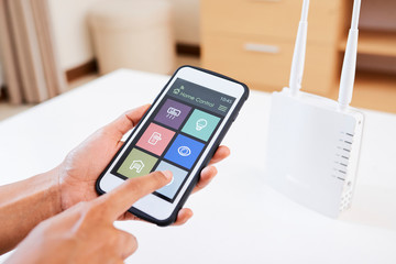 Close-up of woman holding smartphone and connecting smart home system with wi-fi router at home
