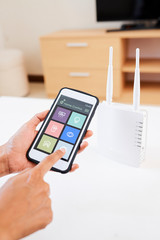 Close-up of woman using smart home system on mobile phone and making setting on wi-fi router at home