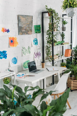 selective focus of selective focus of spacious room with laptop on table, paintings on wall and rack with potted plants