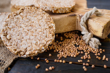 Airy, round, crisp buckwheat crispbread on wooden background with buckwheat scattered around, vintage board and burlap